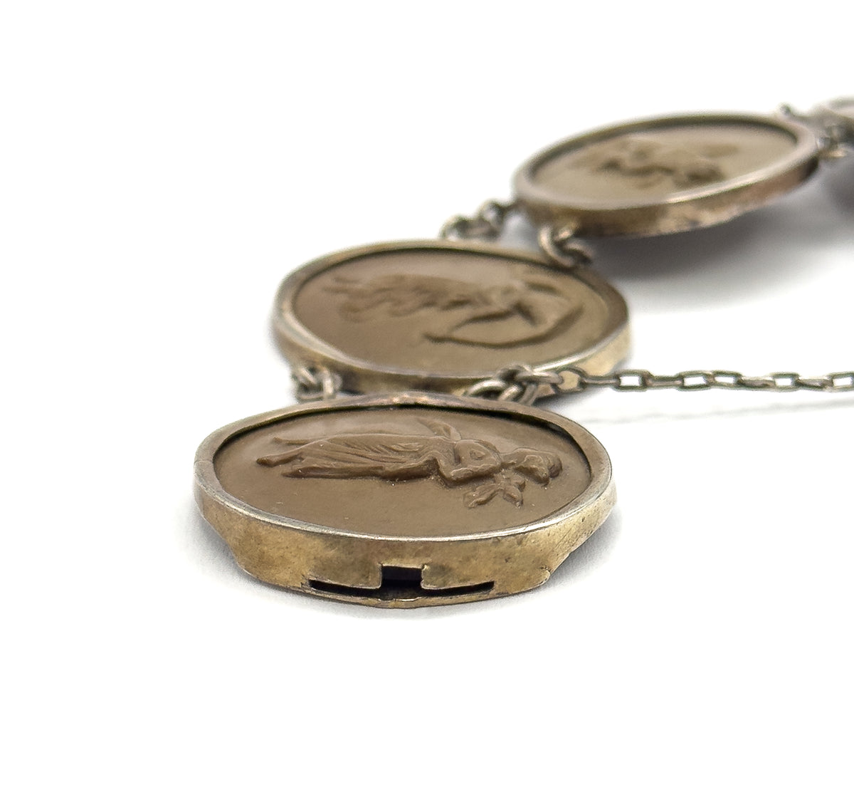 Low raking view along three oval cameos, the nearest showing the slotted side of the hidden box clasp built into its bezel edge, with the safety chain trailing off to the right.