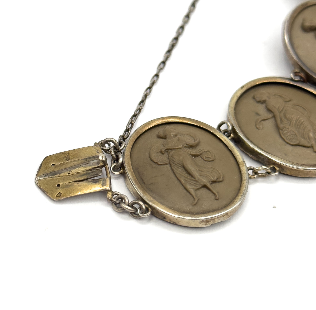 Front view close-up of two carved khaki-brown cameos in their bezels, each showing a draped classical figure, with the flat tongue of the hidden box clasp pulled out at the left and the safety chain looping below.