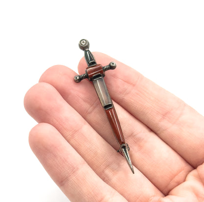 Shown lying diagonally across the fingers of an open palm, full length visible from the rounded pommel through the crossguard to the sharp point.