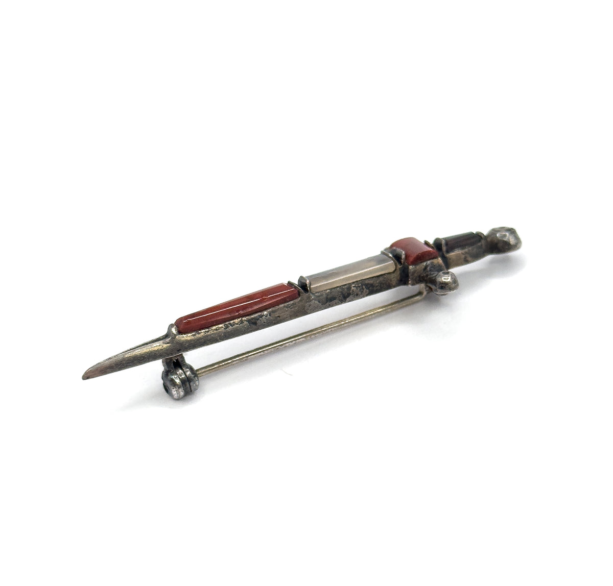 Seen from above at a steep tilt with the pin stem swung clear of the blade, so both the stone-set front and the open pin and its coiled hinge are visible at once.