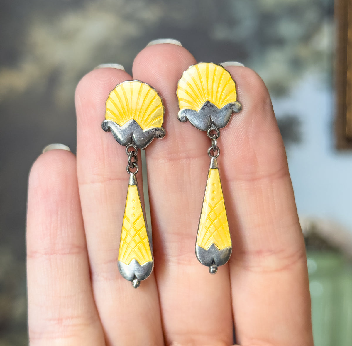 Art Deco yellow enamel seashell drop earrings in sterling silver, shown resting against the fingers of a hand, each fluted shell top linked to a long tapering drop below.