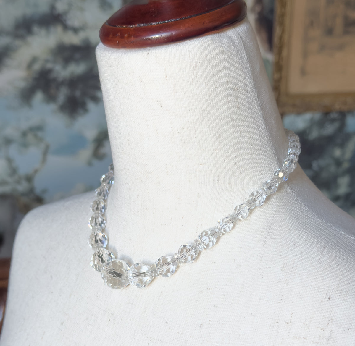 The necklace shown at the neck on a linen dress form, the graduated colourless beads curving from small at the back to the largest at the centre front.