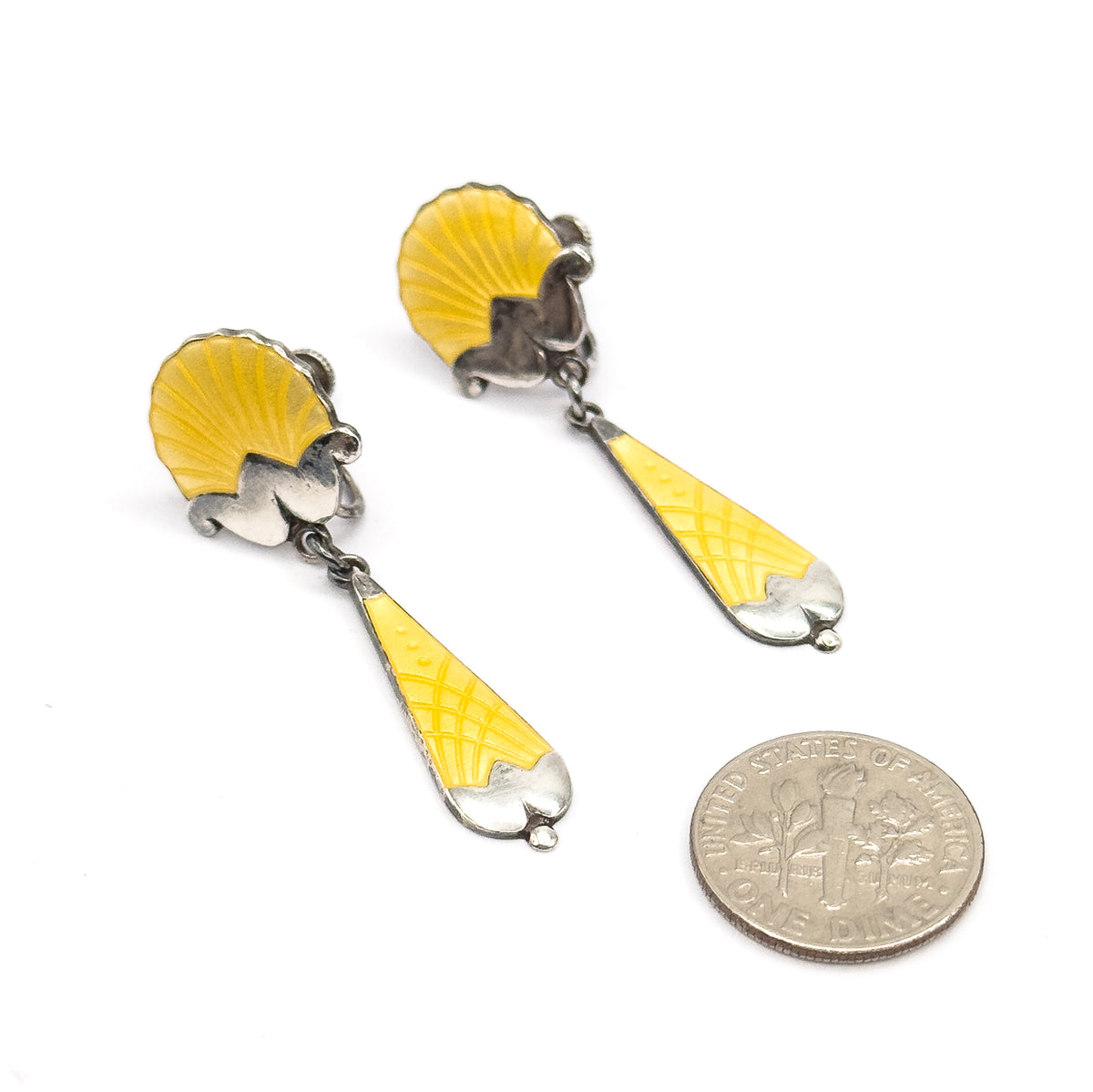 Both earrings lie flat on a white surface beside a dime for scale, the coin roughly matching the length of each yellow enamel drop.