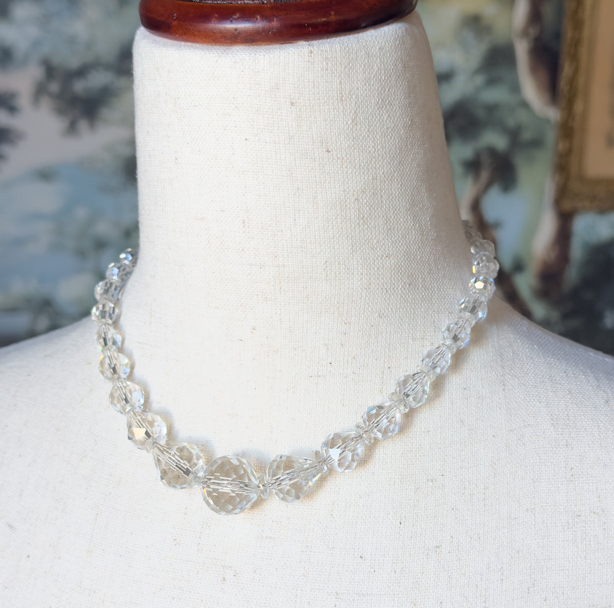 Closer view at the neck on the linen form, showing the largest faceted beads meeting at the centre front with the smaller graduated beads rising toward the back.