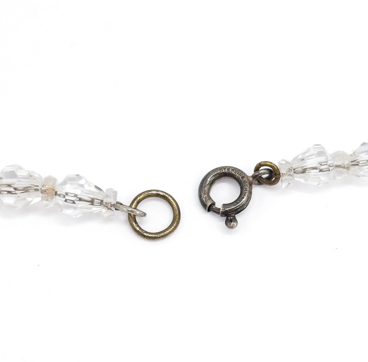Close view of the two open ends against white, showing the darkened sterling silver spring-ring clasp stamped at its edge and the base metal jump ring opposite, each joined to the smallest beads.