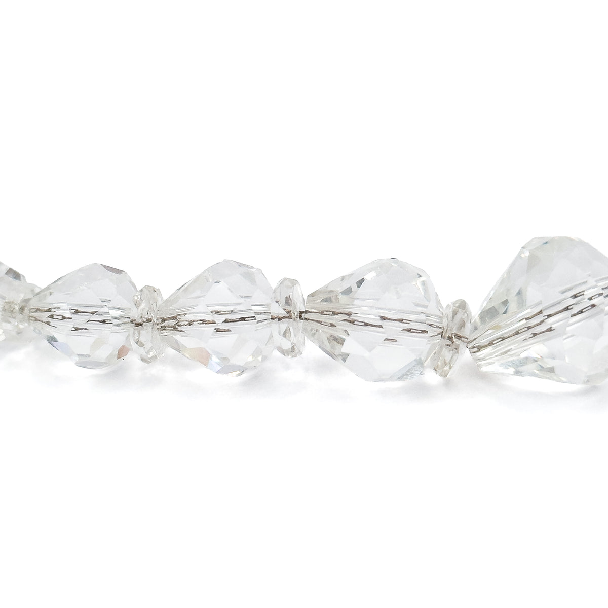 Extreme close-up of a few beads against white, the faceted colourless shapes alternating with small flat disc beads and the stringing cord visible running through each drilled hole.