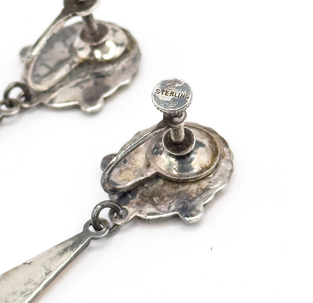 A tight close-up of one screw fitting, its knurled disc stamped STERLING above the threaded post, with the shell reverse, its jump ring and the top of the drop below.
