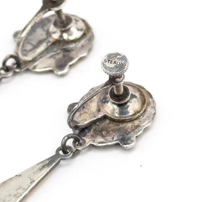 A tight close-up of one screw fitting, its knurled disc stamped STERLING above the threaded post, with the shell reverse, its jump ring and the top of the drop below.