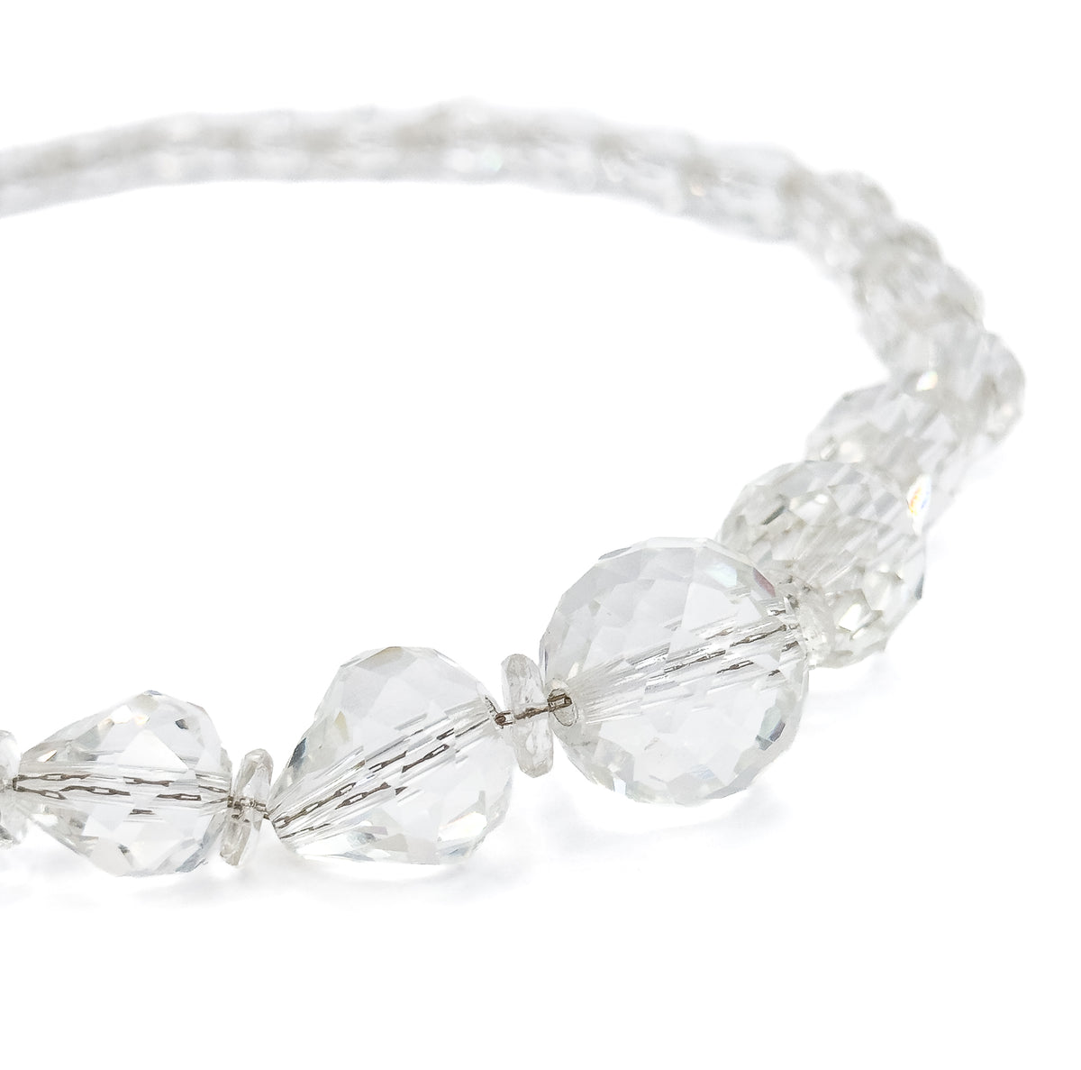 The strand curving across white from the large round and cone-shaped centre beads in the foreground to progressively smaller faceted beads receding into soft focus along the arc.