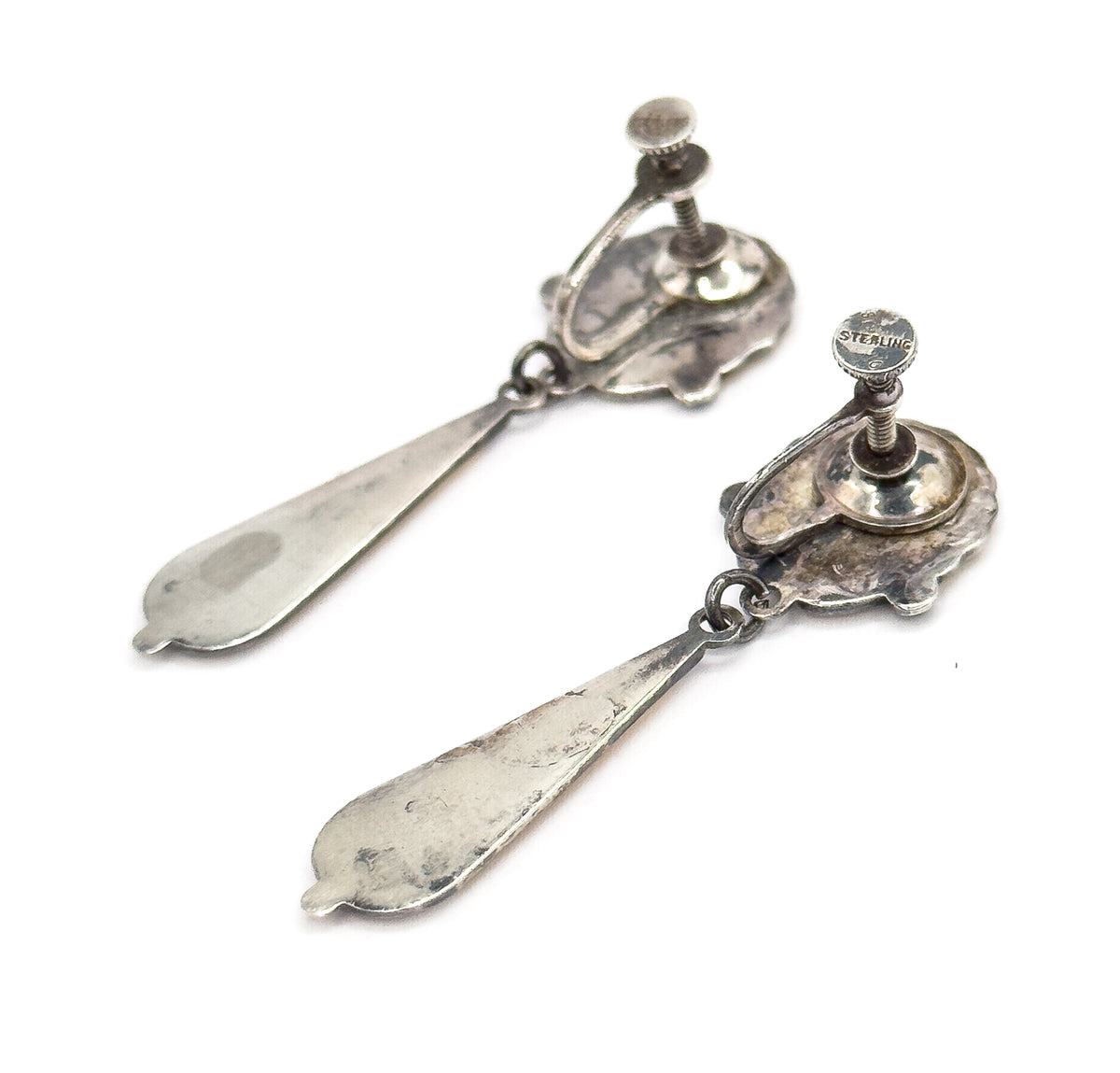 Both earrings seen from behind at an angle, the domed cups and raised screw discs standing proud of the shell backs while the long tapered drops trail away full-length across the white.