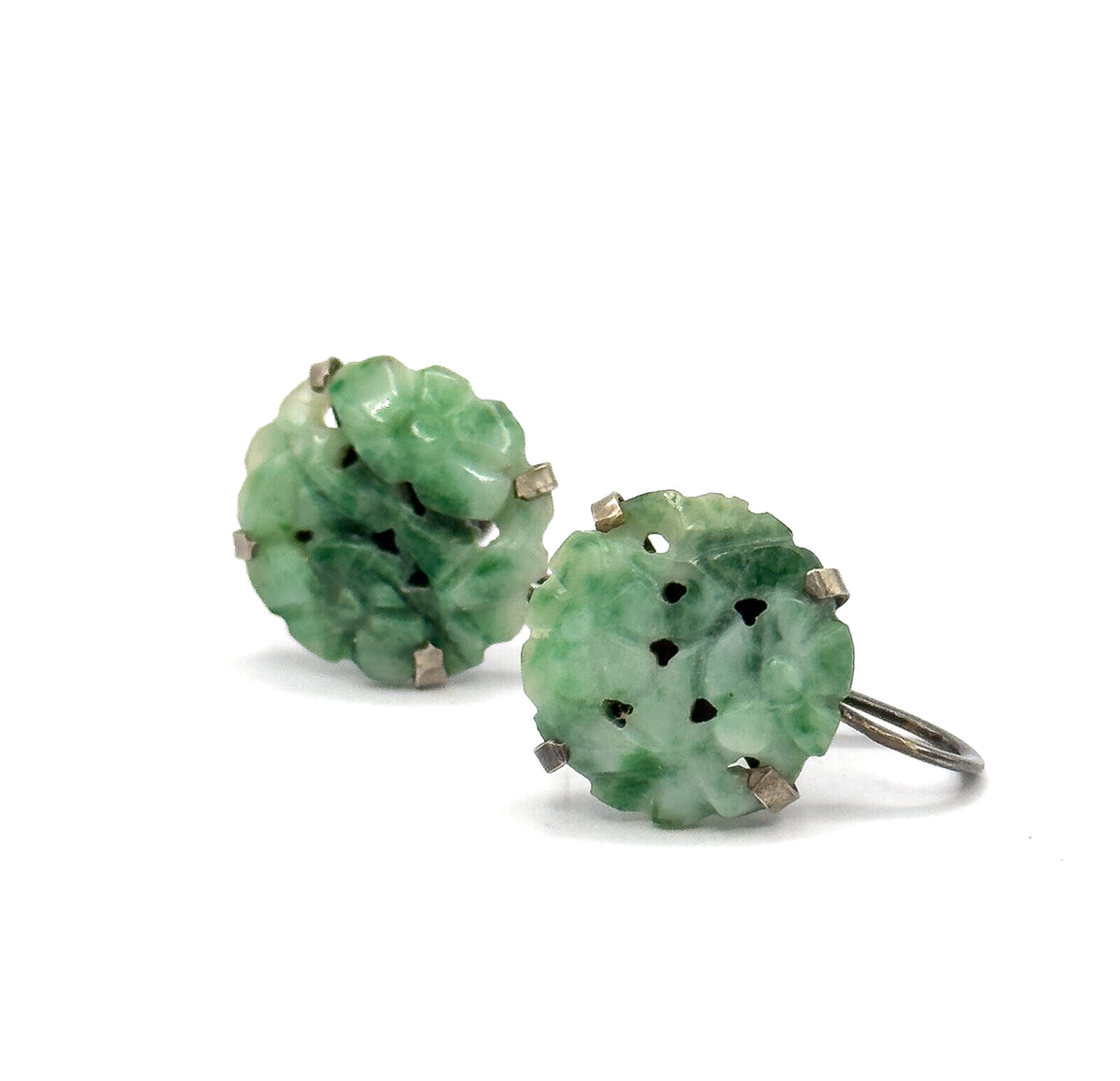 Front view of the pair side by side, the carved floral surfaces and small pierced openings catching the light, with minty to deeper green across the two stones and silver prongs gripping each edge.