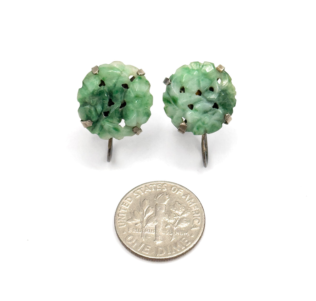 Both earrings upright above a dime for scale, each carved jade disc a little wider than the coin's face, with sterling prongs and screw-back arms curving below.