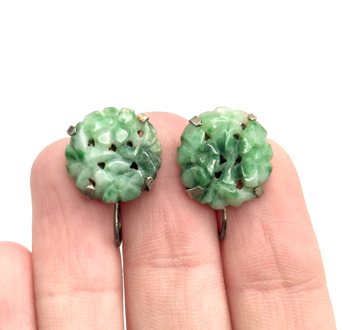 Art Deco carved nephrite jade earrings in sterling silver, the pair rested on fingertips for scale, each round stone held by prongs in a simple bezel above a curved screw-back fitting.