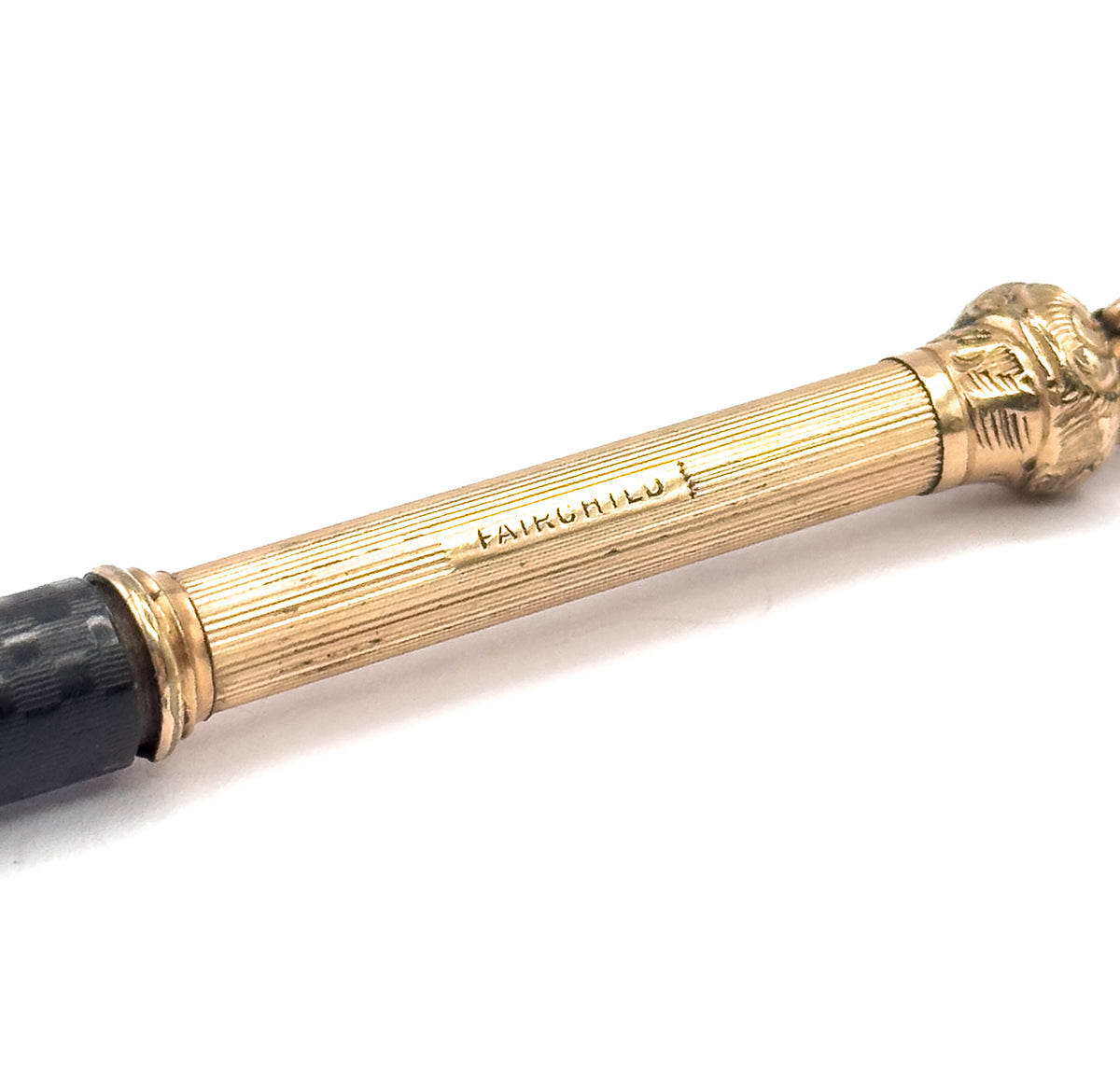 Close crop of the lengthwise-ribbed gold filled cap stamped FAIRCHILD, with its banded collar meeting the black chased rubber barrel at left and the chased cap top at upper right.