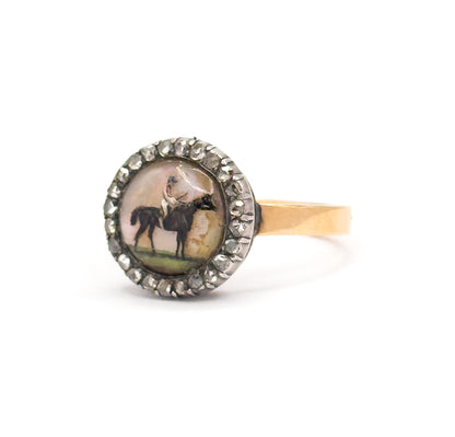 Three-quarter front view on white, the painted horse and rider in the Essex crystal facing the viewer within its silver-set diamond halo, the yellow gold shank angling back to the right.