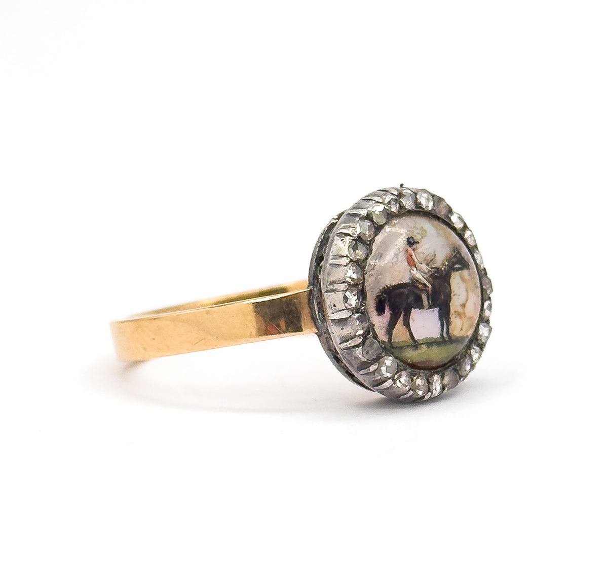 Angled side view on white, showing the depth of the round bezel with its silver-set diamond halo tilted toward the viewer and the flat yellow gold shank sweeping away to the left.