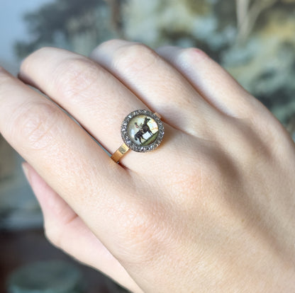 Victorian Essex crystal and rose cut diamond ring in 14K yellow gold, shown on a finger, its domed crystal picturing a man on horseback within a silver-topped halo of tiny diamonds.