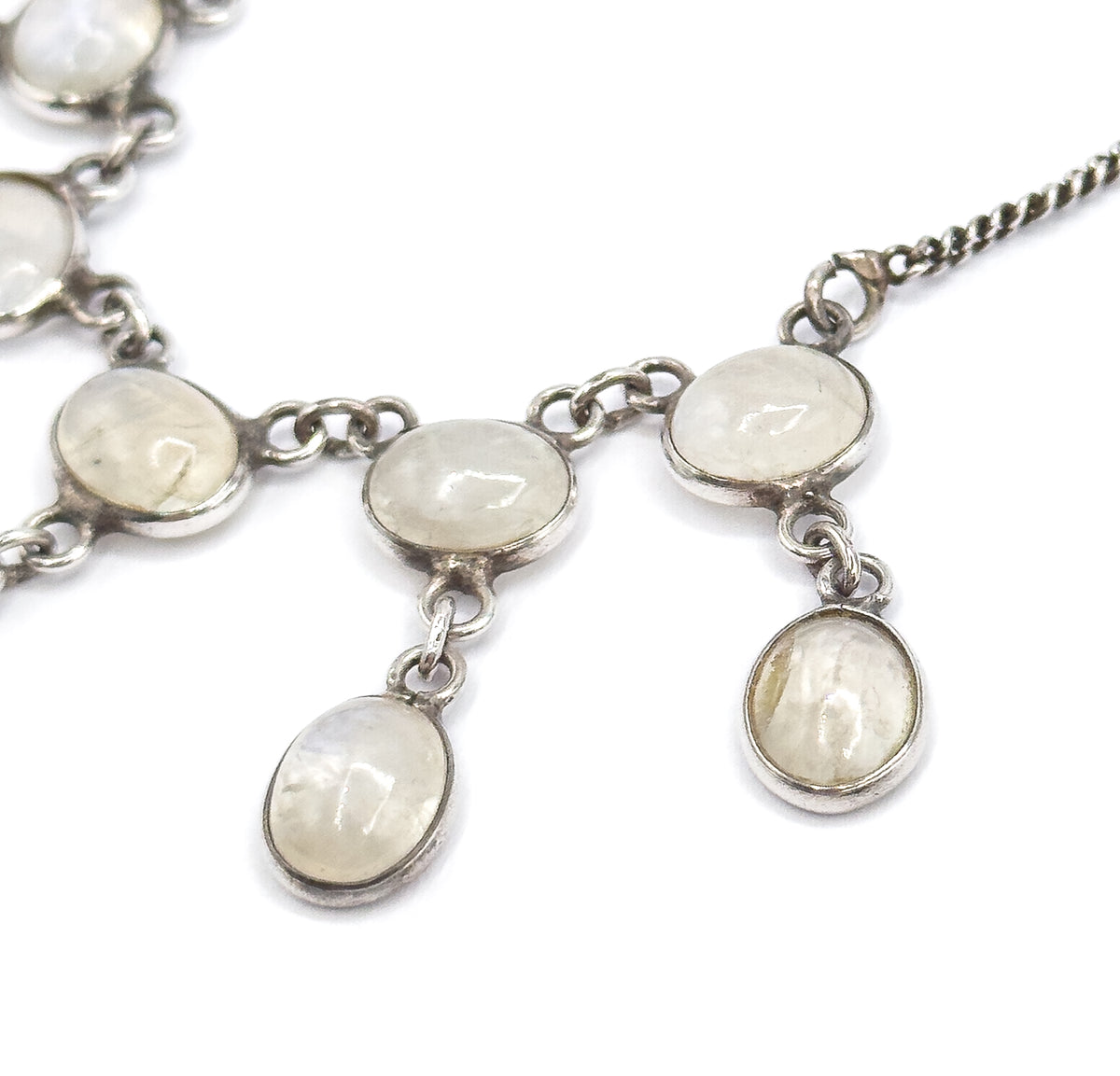 Macro of the fringe's right side where the twisted chain meets the top bezel, three oval moonstone cabochons in a row above two hanging drops, each suspended on its own jump ring.