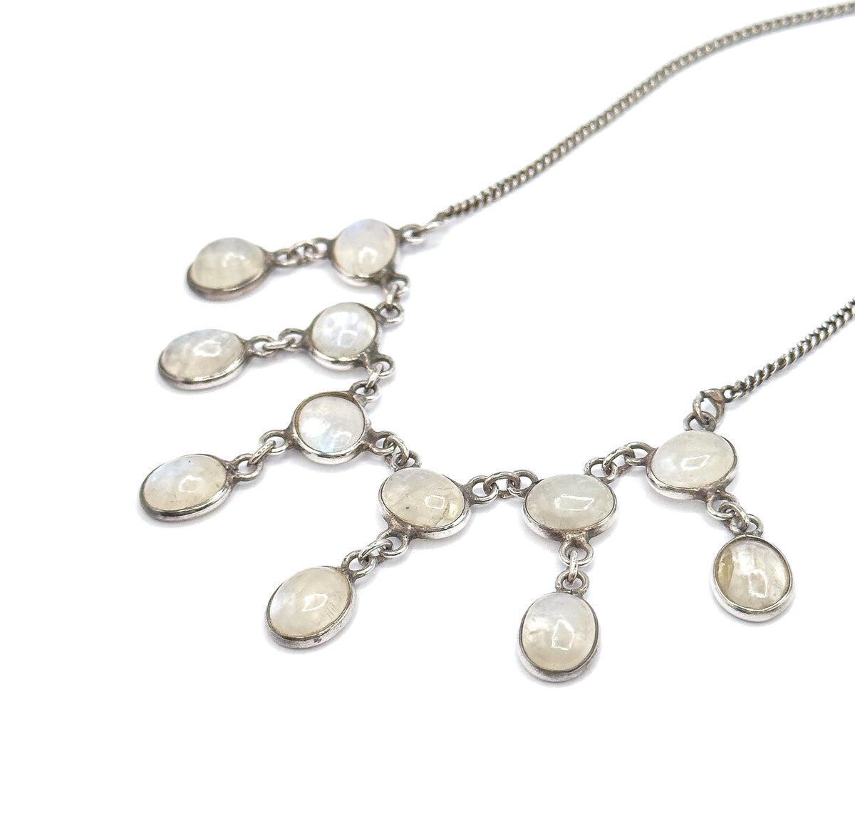 The full fringe seen from above at an angle, both chain ends sweeping off to the upper corners while the bezelled moonstone cabochons fan out in linked tiers across white.