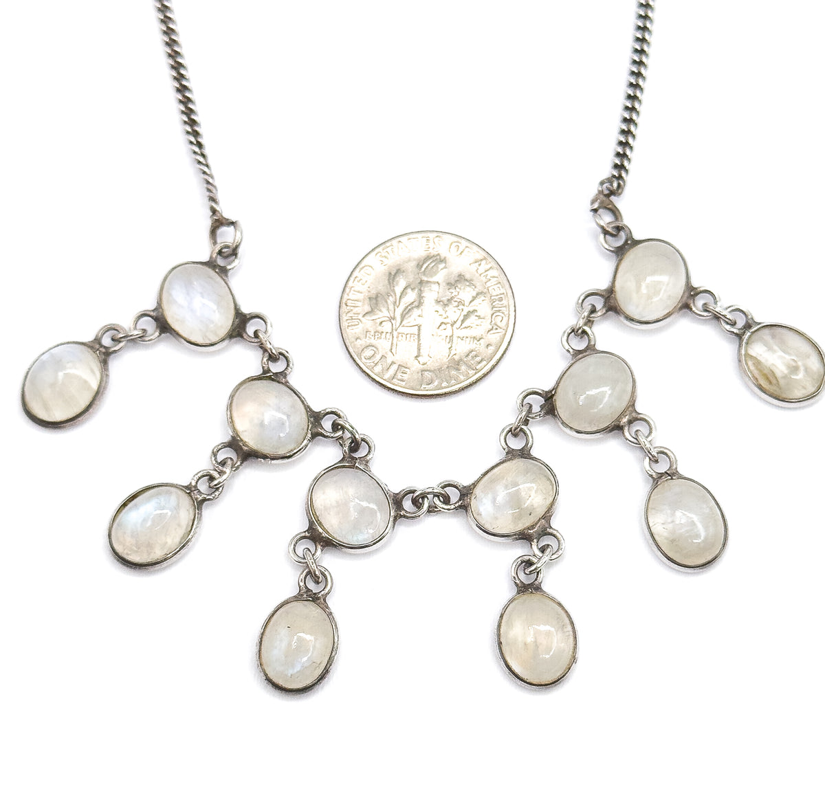 A US dime laid among the linked moonstone bezels for scale, each oval cabochon reading slightly smaller than the coin across the fanned fringe.