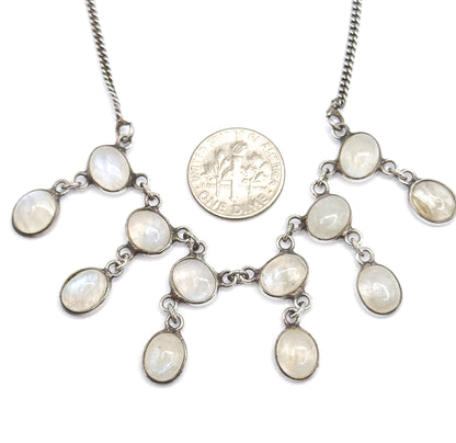 A US dime laid among the linked moonstone bezels for scale, each oval cabochon reading slightly smaller than the coin across the fanned fringe.