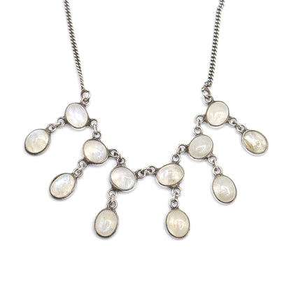 Straight-on symmetrical view of the whole fringe centred on white, the curb chain rising to both upper corners while the oval moonstone bezels mirror each other in linked, stepped tiers.