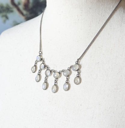 Shown at the neck on a cream linen bust form, the fringe of bezel-set oval moonstone drops curving across the collarbone with the fine chain rising to either shoulder.