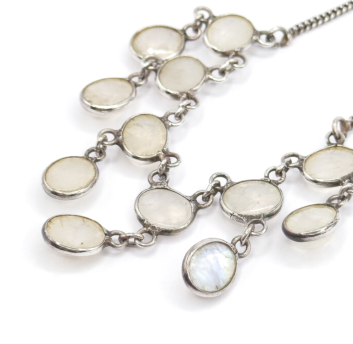 Macro on a white background showing the oval moonstone bezels and their connecting links in detail, with blue flash lighting the lowest centre drop.
