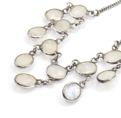 Macro on a white background showing the oval moonstone bezels and their connecting links in detail, with blue flash lighting the lowest centre drop.