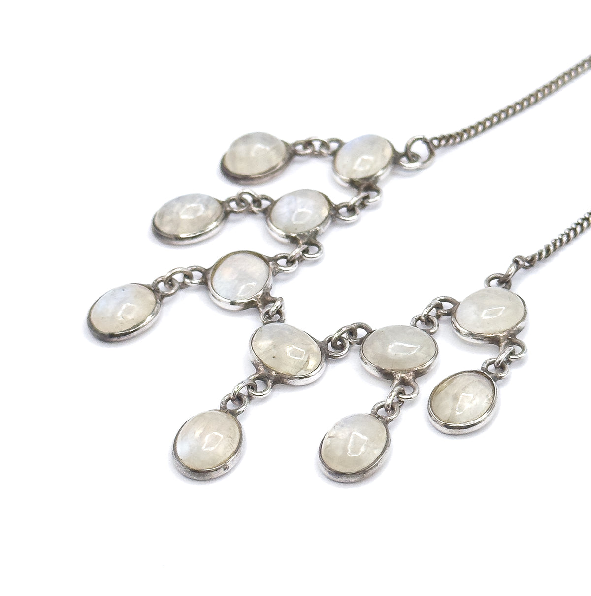 Angled side view on white with the fringe seen obliquely, so the depth of each bezel wall and the small jump rings joining stone to stone are visible along both chain ends.