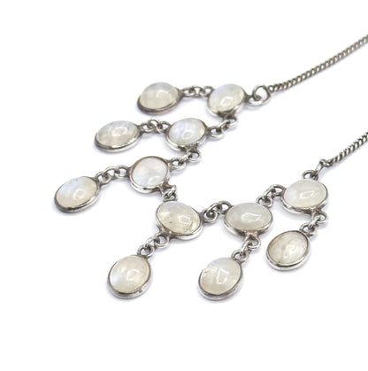 Angled side view on white with the fringe seen obliquely, so the depth of each bezel wall and the small jump rings joining stone to stone are visible along both chain ends.