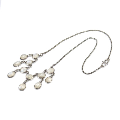 The whole necklace laid open on white, the curb-link chain forming a long loop with the S-hook clasp at one end and the twelve-stone moonstone fringe gathered at the other.