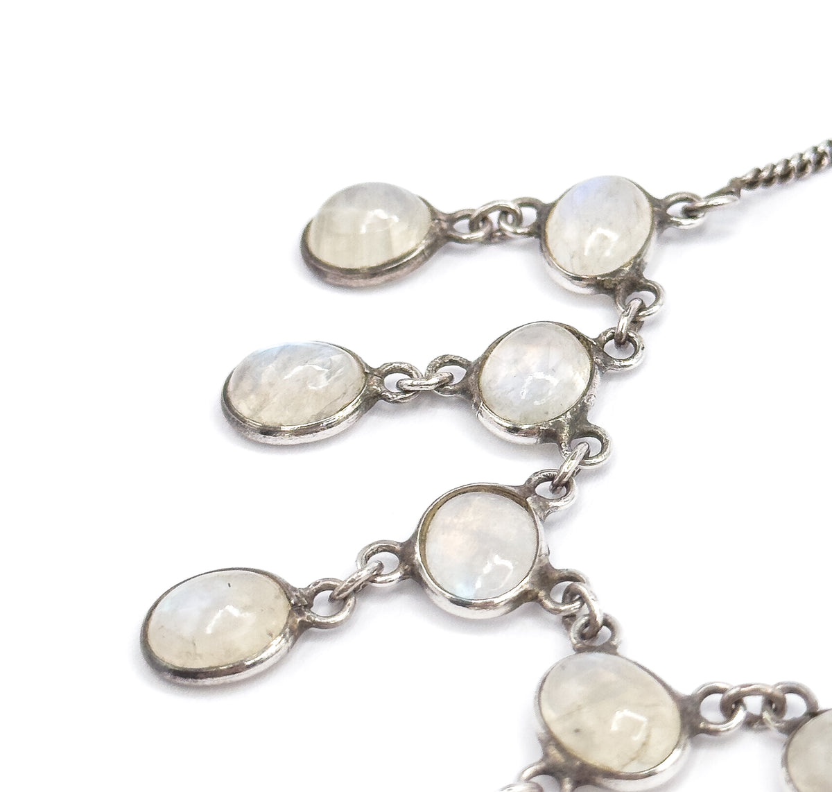 Close crop on the upper fringe where the curb-link chain enters at the top right, the bezelled moonstones stepping diagonally down in pairs on their jump rings against white.