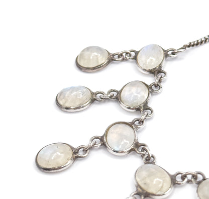 Close crop on the upper fringe where the curb-link chain enters at the top right, the bezelled moonstones stepping diagonally down in pairs on their jump rings against white.