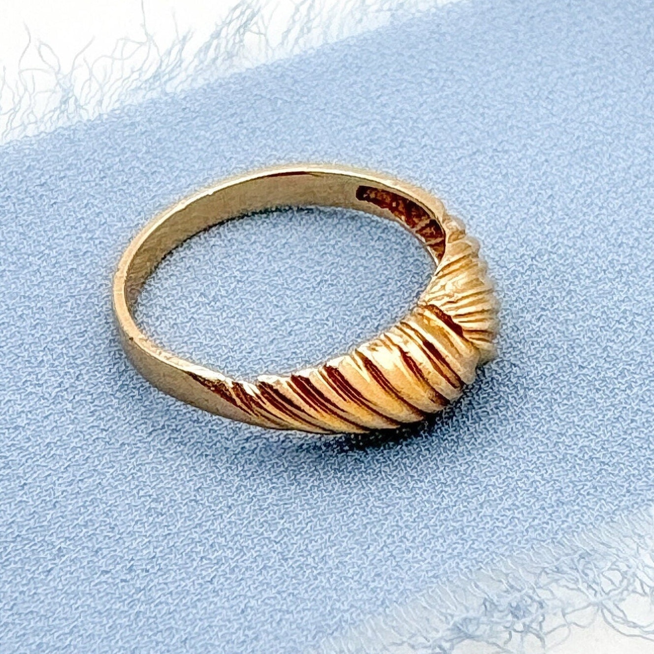 Gold ring with a textured design on a light blue fabric background