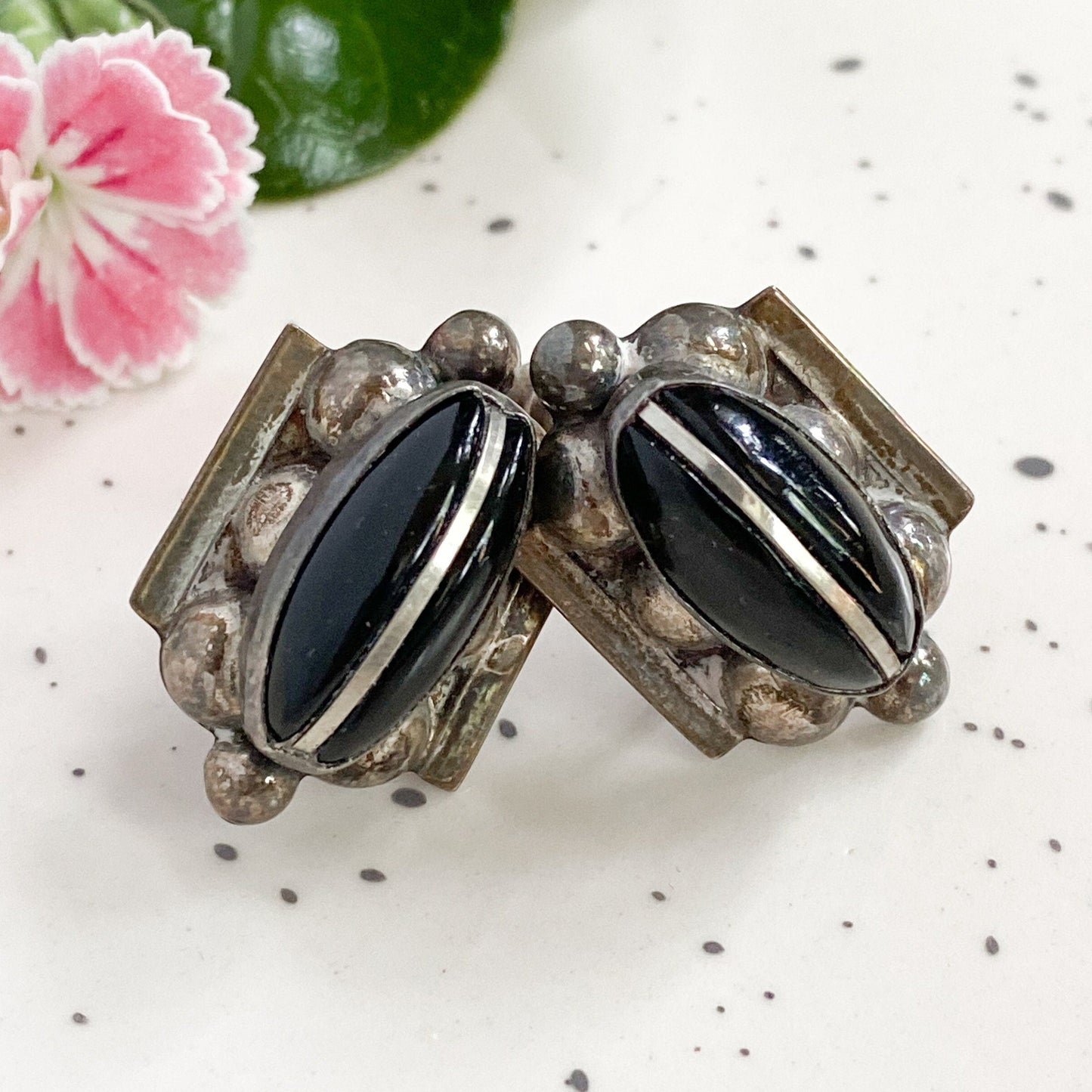 Pair of vintage-style earrings with black stones on a speckled surface with flowers in the background