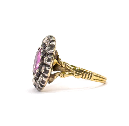 Standing upright with the face angled away, a sliver of the pink sapphire shows between the silver prongs of the halo while the grooved gold shank sweeps right in full view.