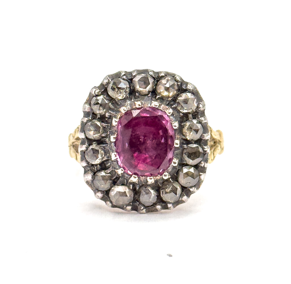 Face-on and level, the cushion-cut pink sapphire glows at the centre of its silver-set halo of fourteen small diamonds, with the foliate gold shoulders just visible at either side.