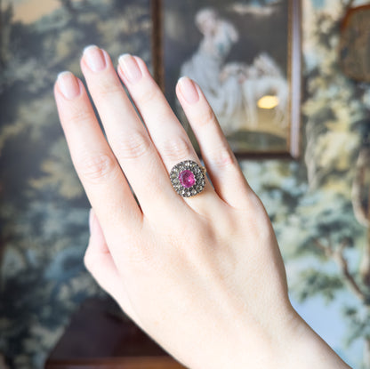 The whole hand is shown raised against a painted backdrop, the ring small on the ring finger, which gives a clear sense of the face's scale next to the width of the finger.