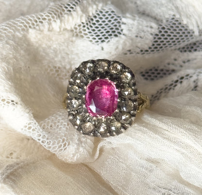 Resting on crumpled white lace, the ring tilts face-up so the pink sapphire and its darkened silver halo fill the frame, one foliate gold shoulder and the shank edging out to the right.