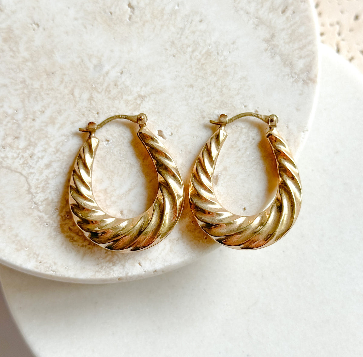 Overhead view of the two hoops lying side by side on a round white dish, showing the full oval shape of each, narrow at the hinged top and swelling into the thick ribbed twist at the base.