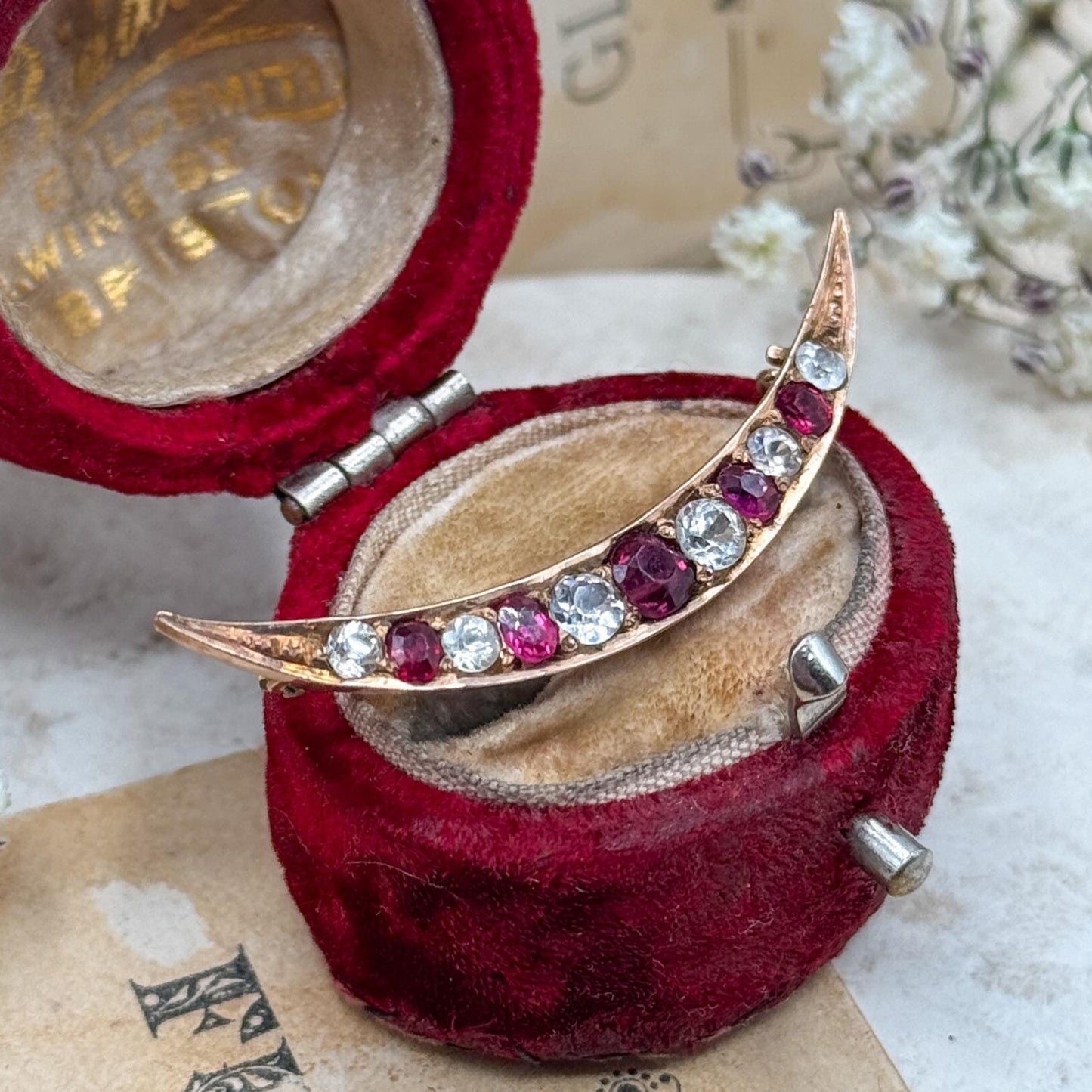 Ornate brooch in a red velvet box on an old book with floral background