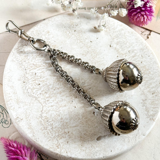 Decorative keychain with acorn-like ends on a white plate with flowers in the background