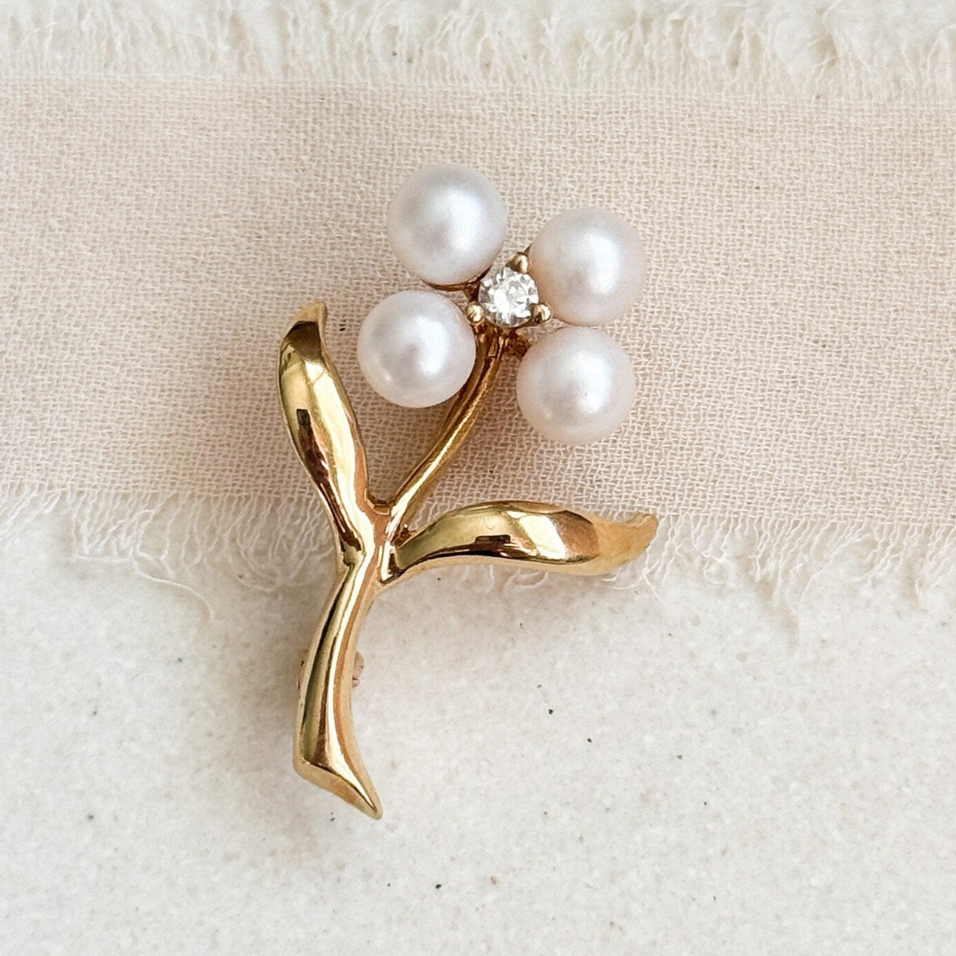 Gold brooch with pearls on a textured beige fabric background