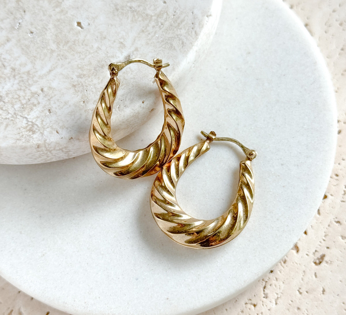 The pair set diagonally across the rim of a round white dish, one hoop below the other, showing the puffy thickness of the ribbed twist in profile and the catch wires closed at the tops.