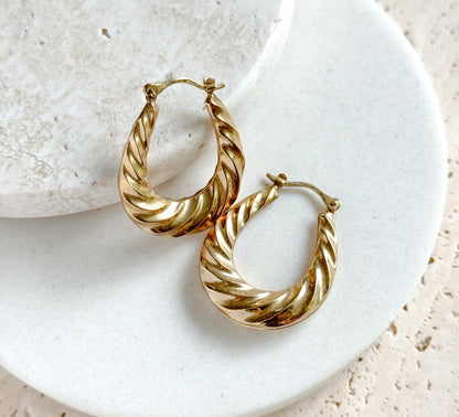 The pair set diagonally across the rim of a round white dish, one hoop below the other, showing the puffy thickness of the ribbed twist in profile and the catch wires closed at the tops.