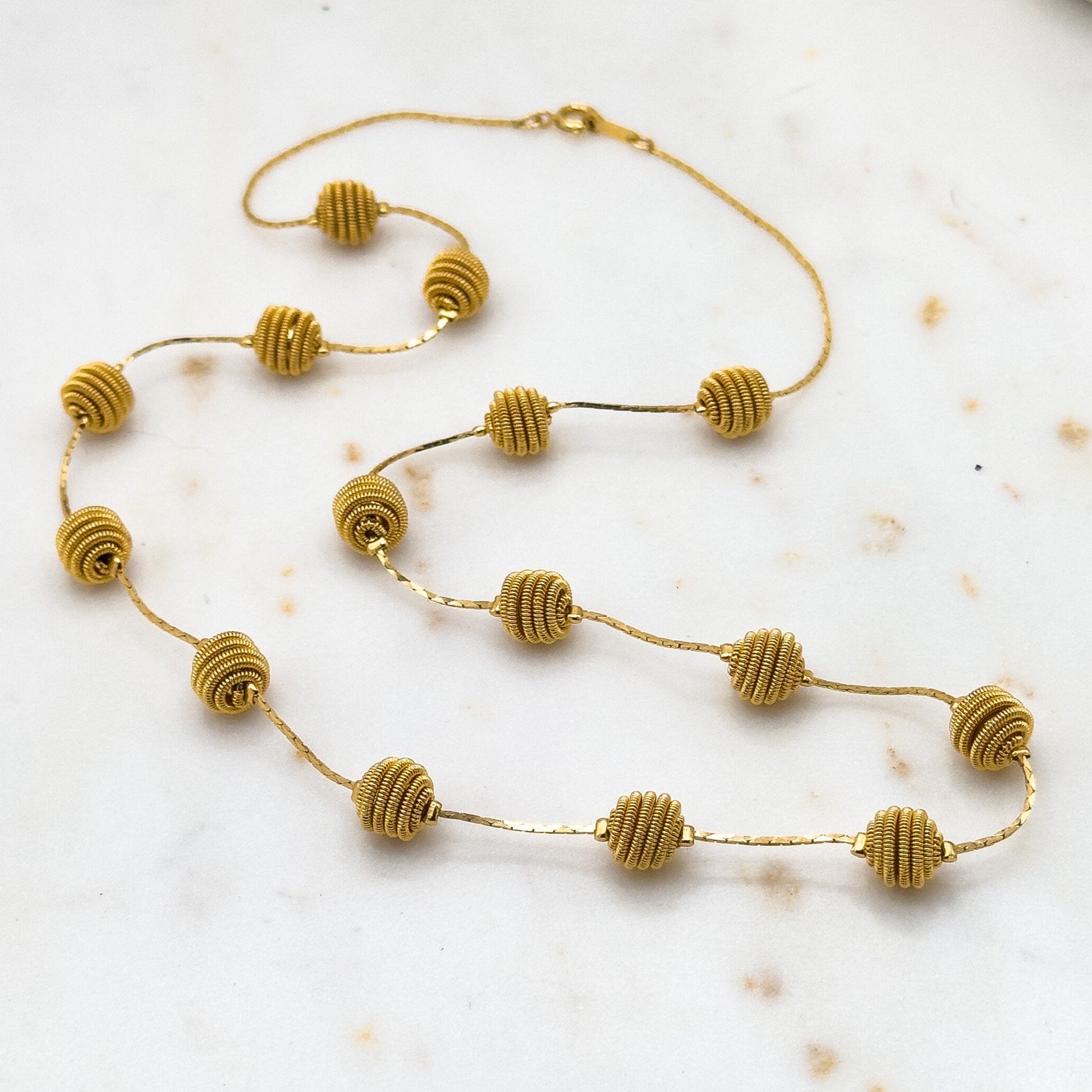Gold necklace with beaded design on a light marble surface