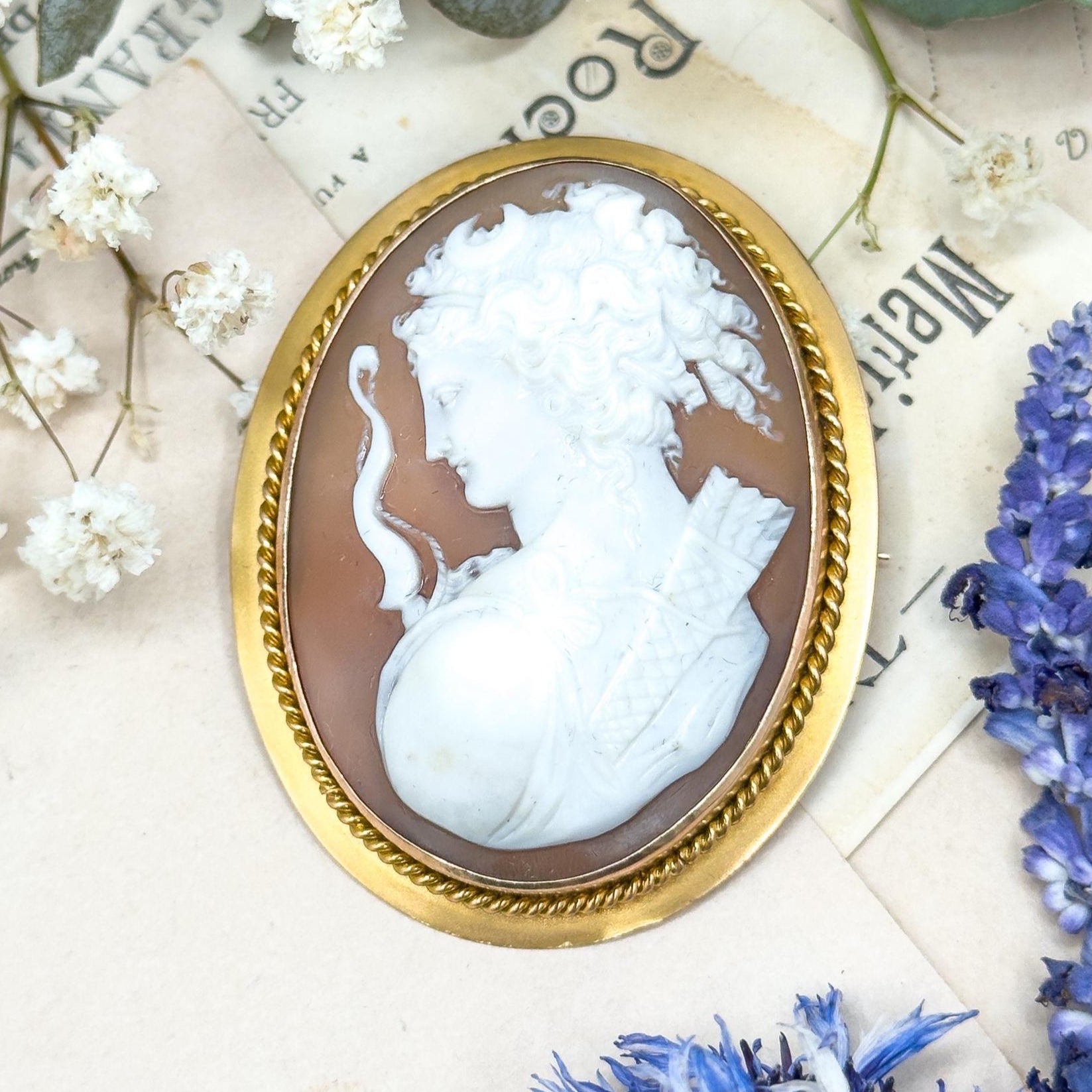 Vintage-style cameo brooch with gold frame on a decorative surface with flowers