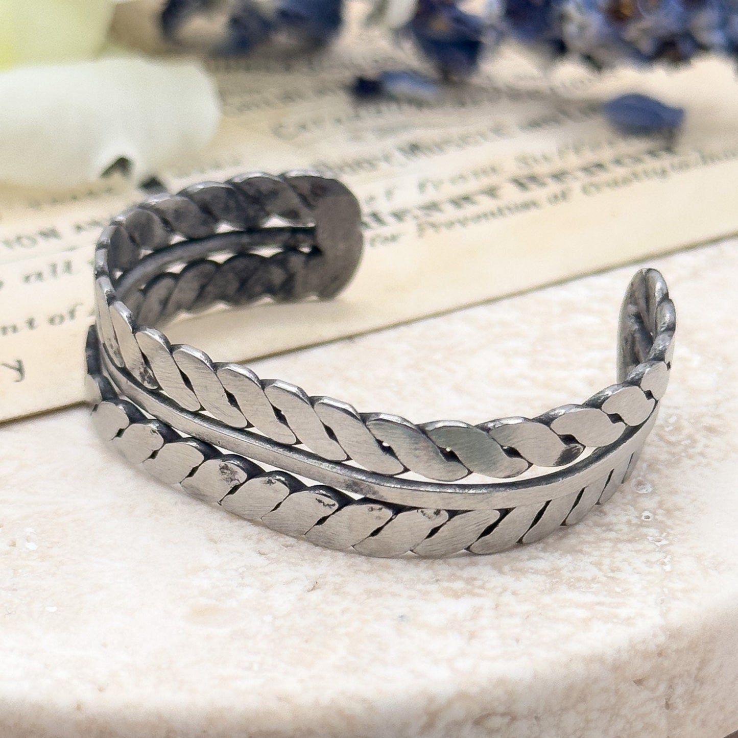 Silver bracelet on a marble surface with flowers in the background Native American Childs bracelet cuff