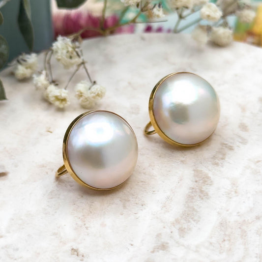 Pearl earrings with gold settings on a textured surface with flowers in the background